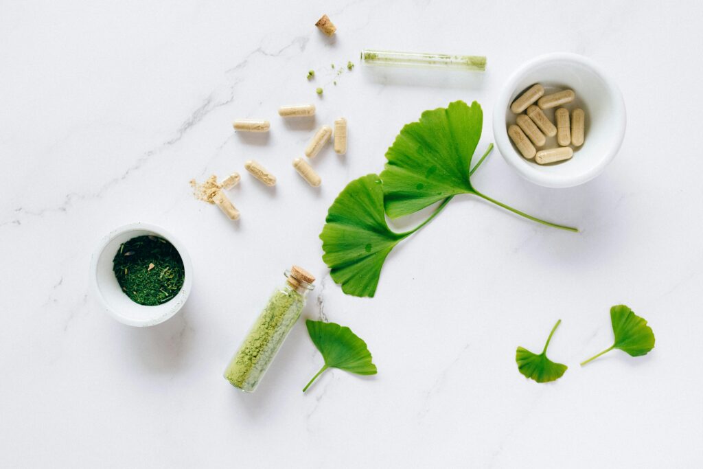 Flat lay of herbal supplements with ginkgo leaves on marble surface, emphasizing natural health remedies.