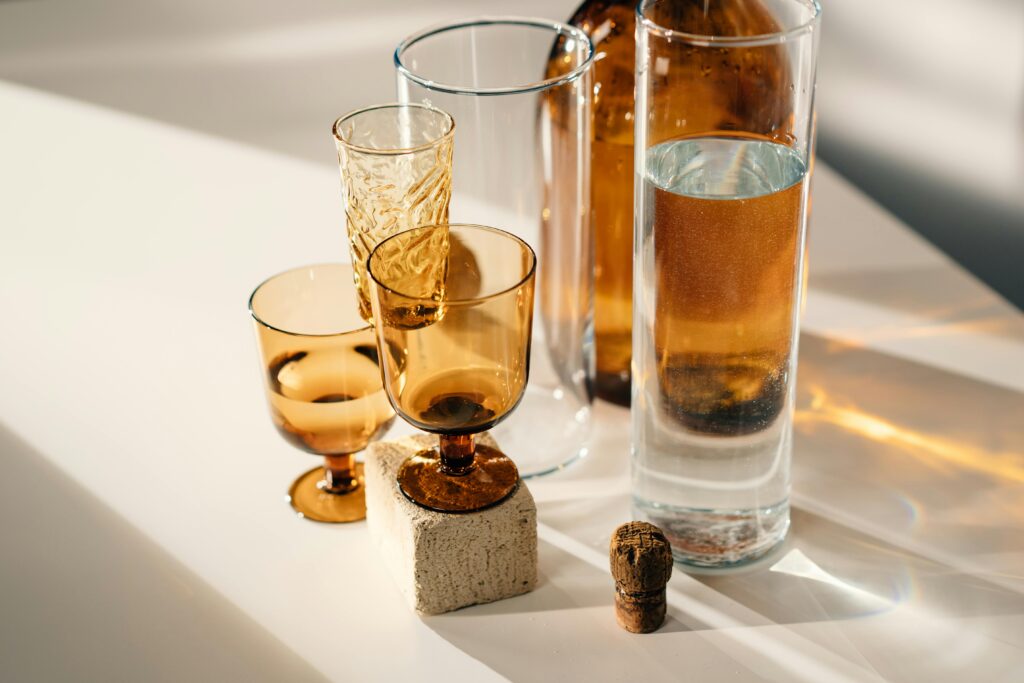 A stylish arrangement of amber and clear glassware with warm shadows on a sunlit white surface.